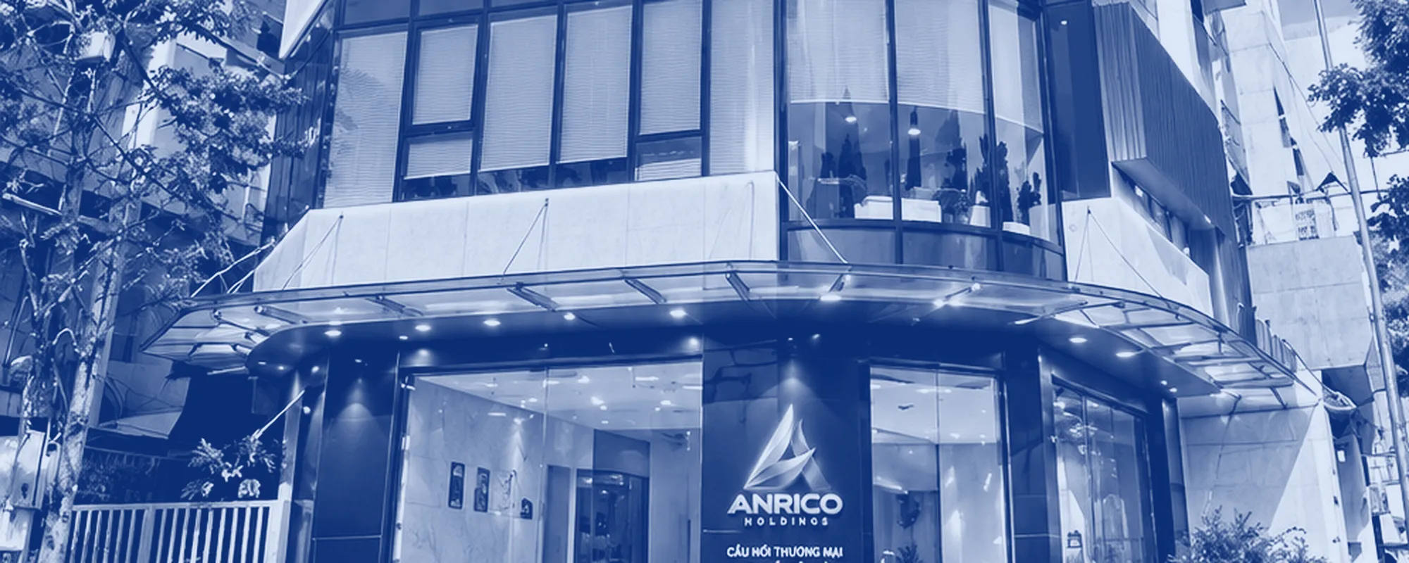 Mặt tiền tòa nhà trụ sở ANRICO HOLDINGS: mái đón, mặt kính tầng dưới và hàng cây bên đường