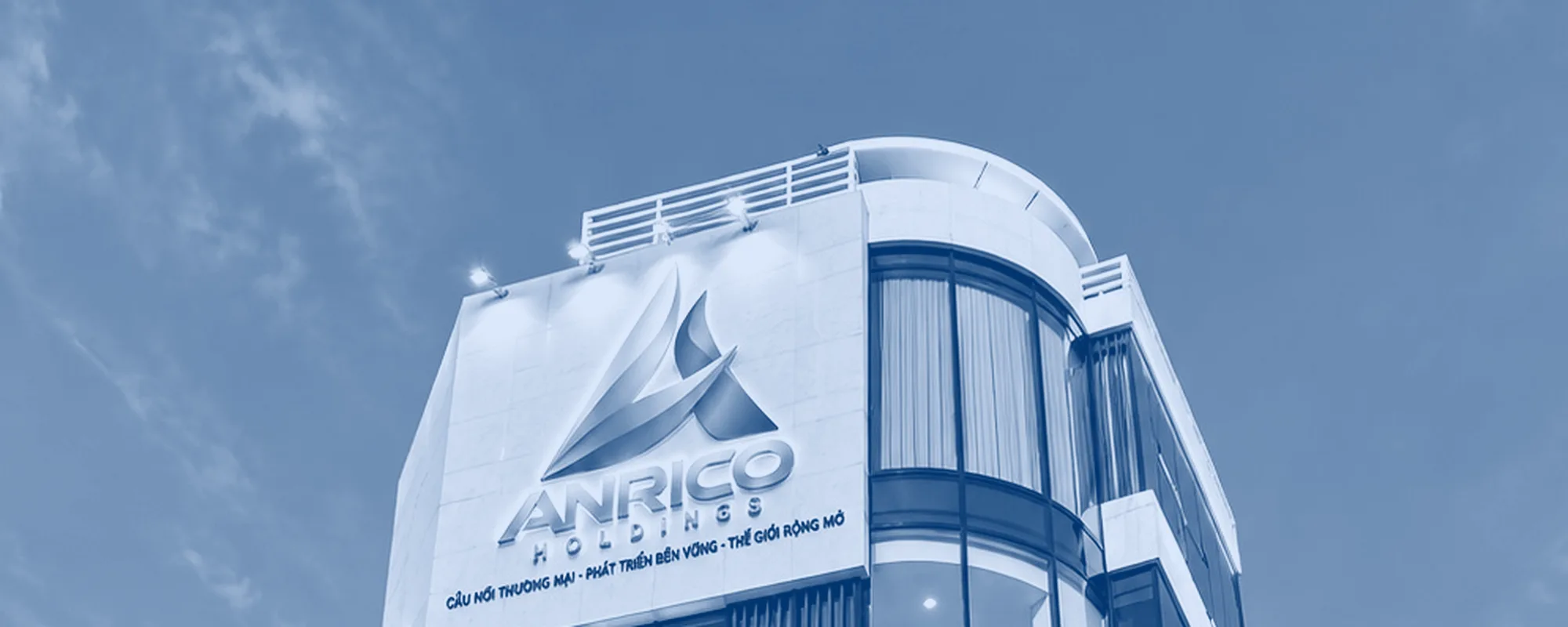 Biển hiệu ANRICO HOLDINGS đặt trên tầng cao nhất tòa nhà trụ sở, nhìn từ góc đường